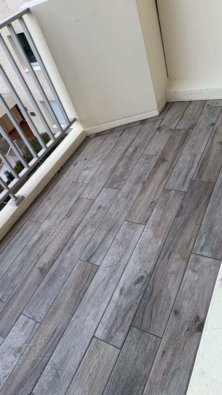 Vue d’ensemble d’un balcon recouvert d’un carrelage gris à effet bois.
