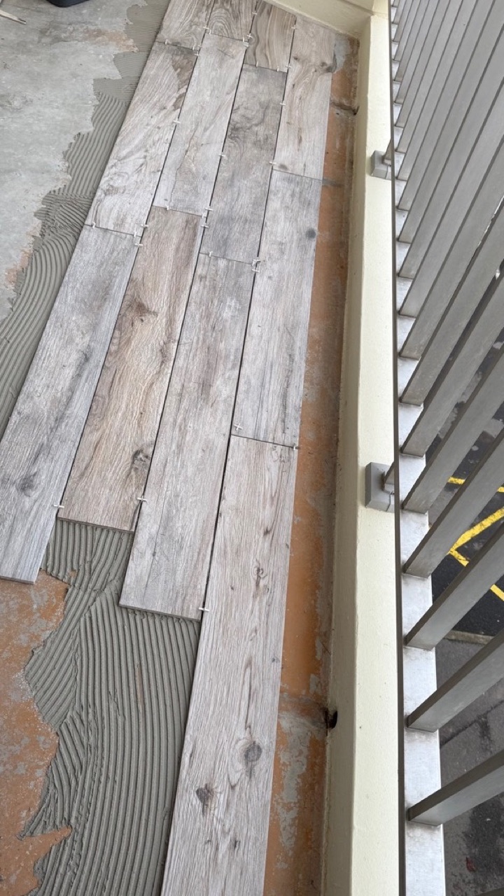 Pose en cours d’un carrelage effet bois sur un balcon avec croisillons d’espacement.