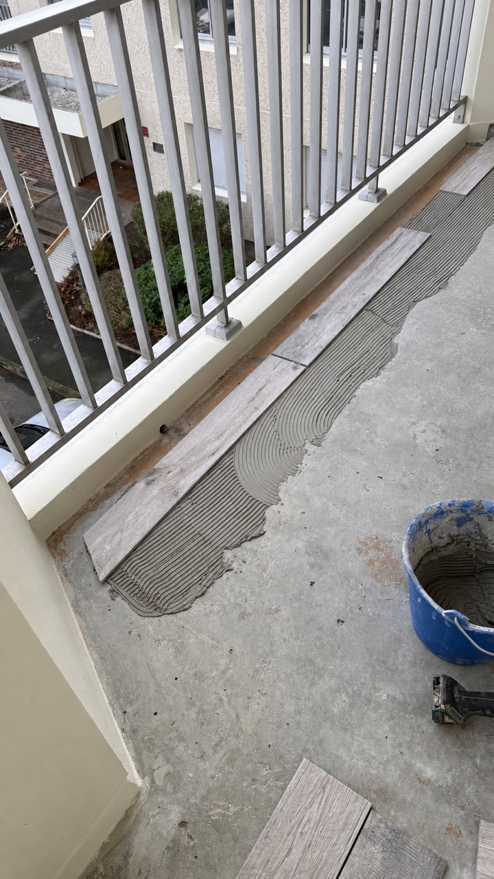 Préparation d’un balcon avec encollage du support avant la pose d’un carrelage effet bois.