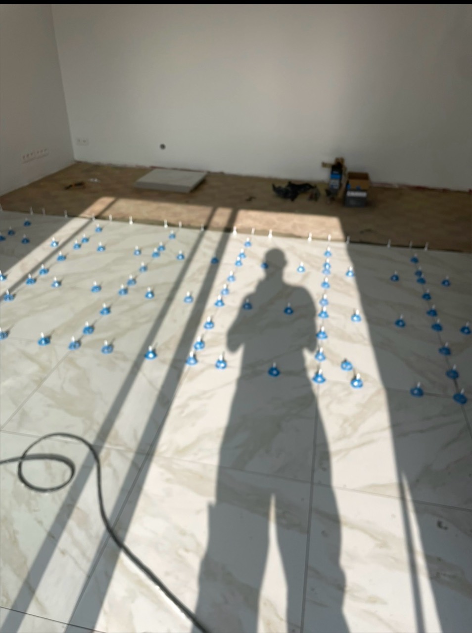 Pose de carrelage grand format avec un système de nivellement visible.