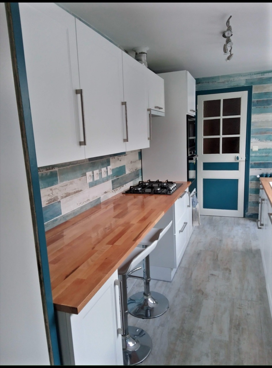 Cuisine équipée avec meubles blancs, plan de travail en bois et espace de cuisson.