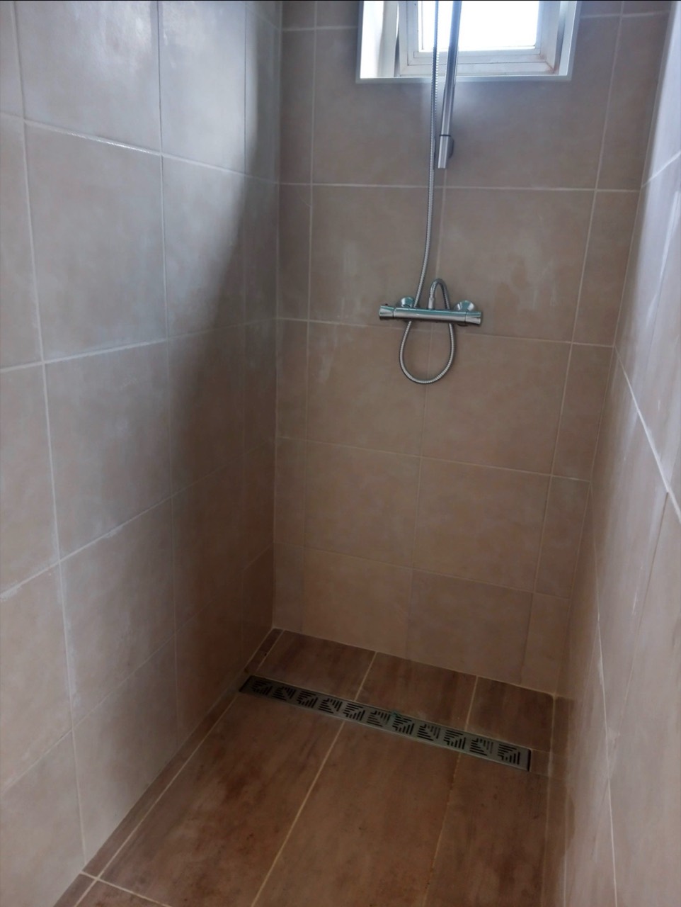 Espace douche entièrement carrelé avec caniveau d’évacuation linéaire.