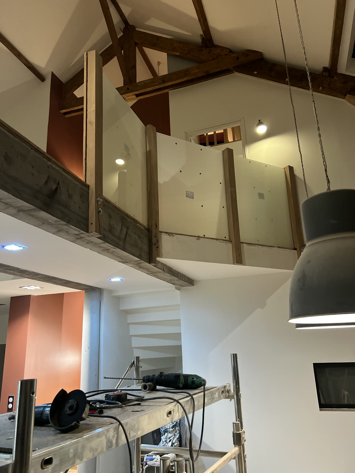 Mezzanine en cours d’aménagement avec charpente bois apparente, garde-corps translucide et échafaudage.