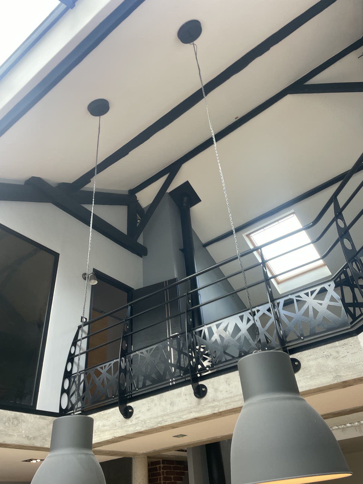 Vue en contre-plongée d’un intérieur avec poutres noires, garde-corps de mezzanine et fenêtres de toit.