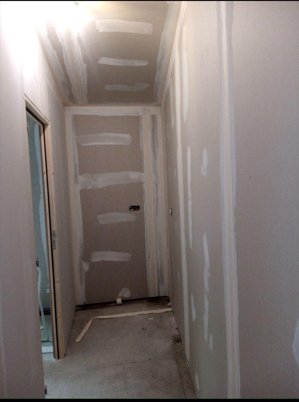 Traitement des joints sur les murs et le plafond d’un couloir rénové.