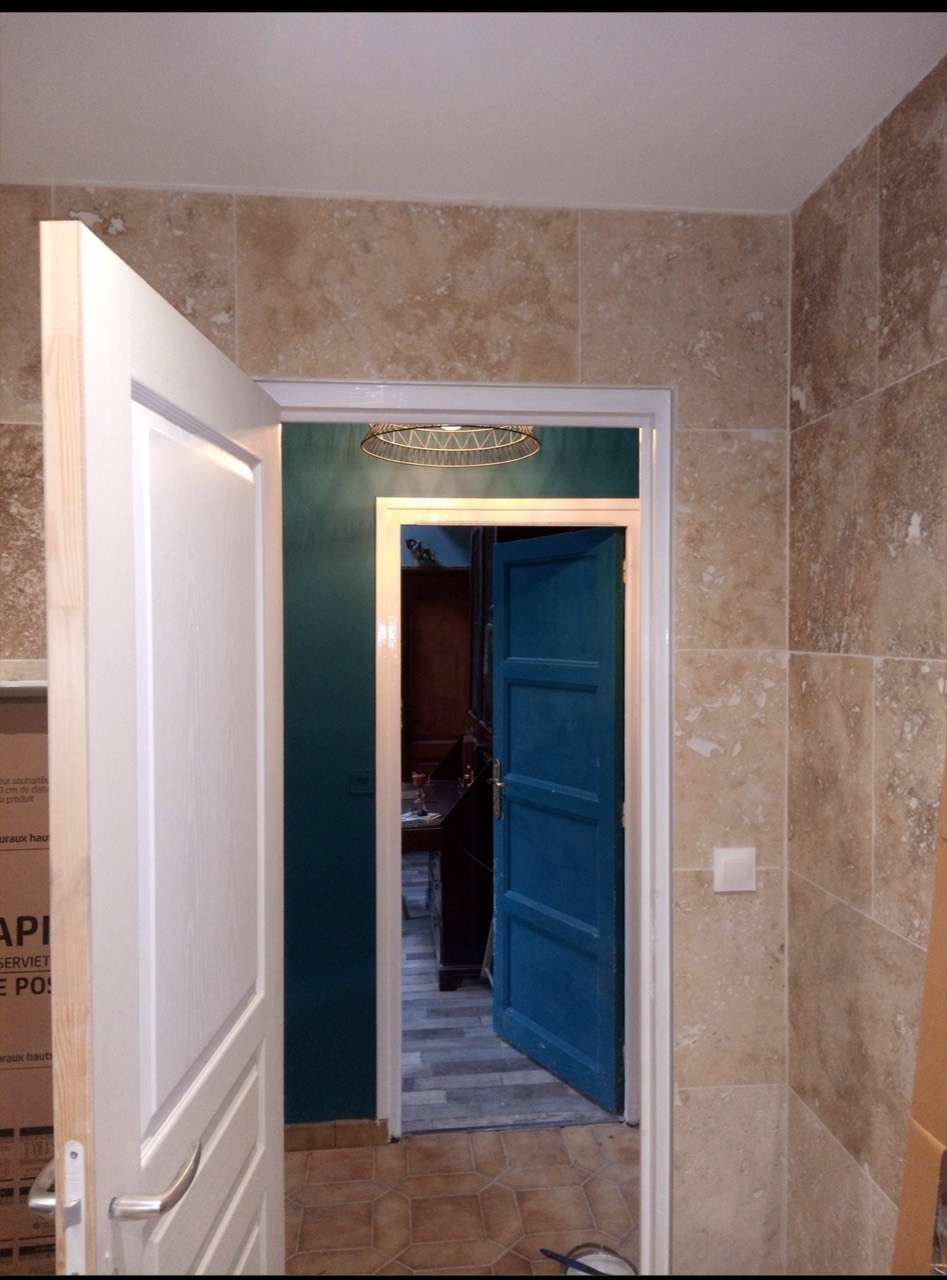 Salle de bain carrelée aux tons pierre vue depuis le passage d’une pièce voisine.