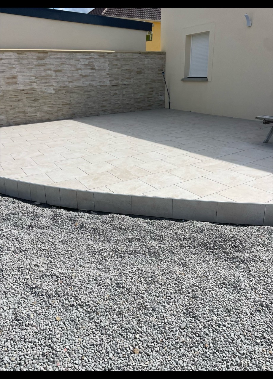 Terrasse extérieure carrelée avec une bordure droite et un parement mural.